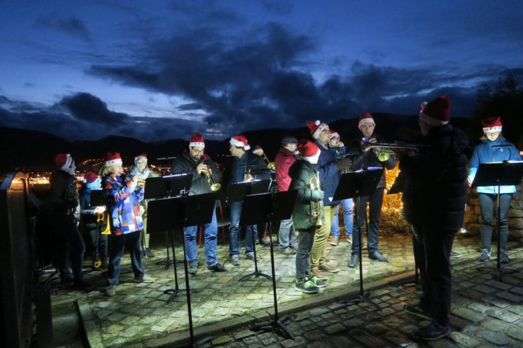Photo des musiciens de l’Ensemble de Cuivres avec leurs bonnets lumineux de Père Noël et en fond les lumières de la ville et celles du ciel peu après le coucher du soleil